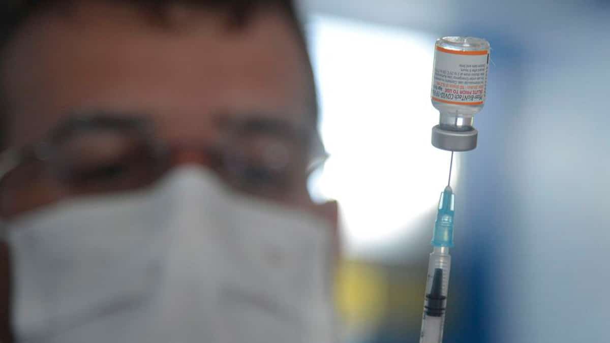 Enfermeiro carregando dose da vacina bivalente contra Covid numa agulha de injeção