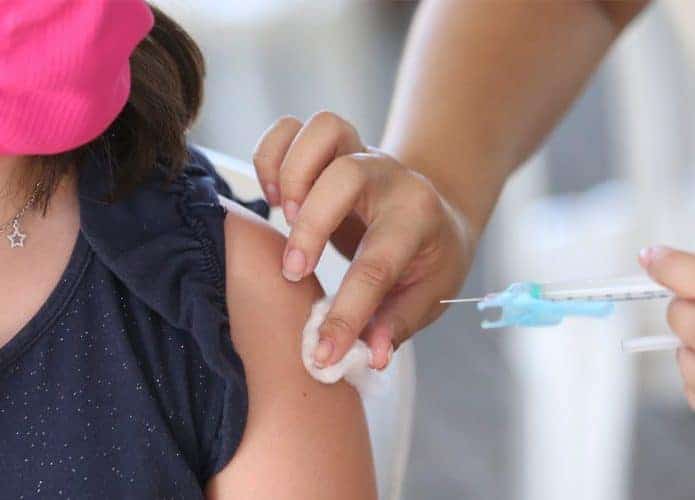 Enfermeira aplicando vacina contra Covid em braço de mulher