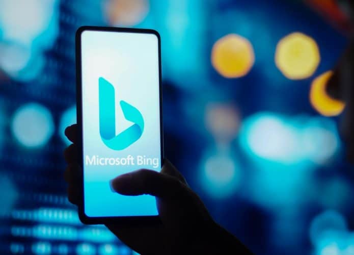 Silhueta de uma mulher segura um celular com o logotipo do Microsoft Bing exibido na tela