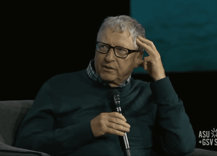 Bill Gates sentado segurando microfone durante evento