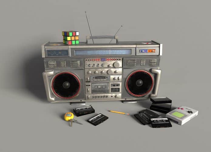Rádio com cubo mágico em cima e fitas, GameBoy, Tamagochi e lápis na frente
