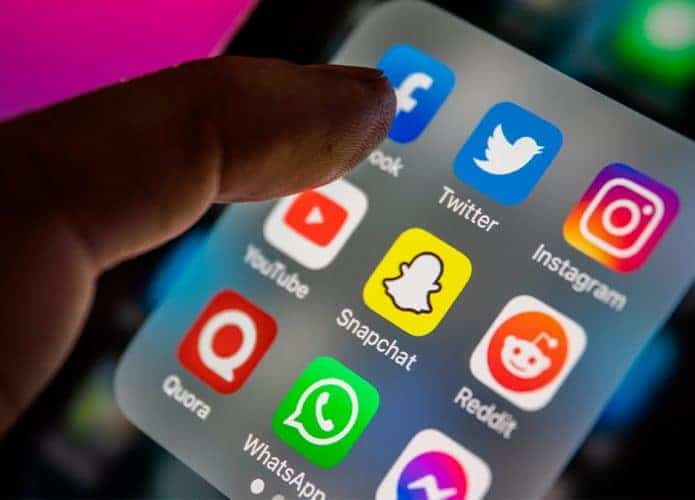 Pessoa com dedo acima de ícones de redes sociais em iPhone