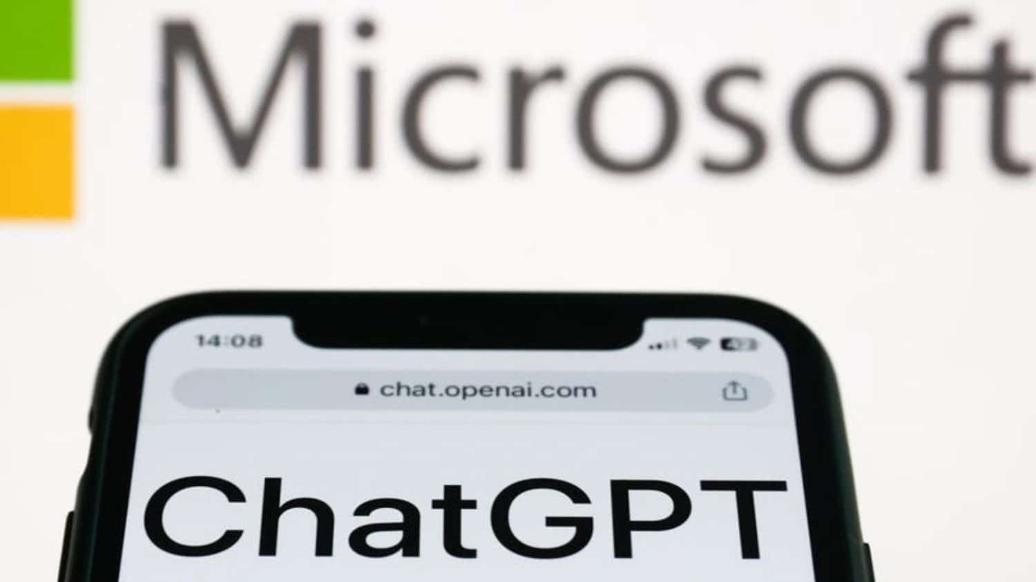 Página do ChatGPT aberta num iPhone em frente tela de computador com imagem da logomarca da Microsoft aberta