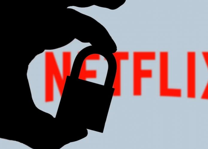 Pessoa segurando cadeado trancado e, ao fundo, logomarca da Netflix exibida numa tela