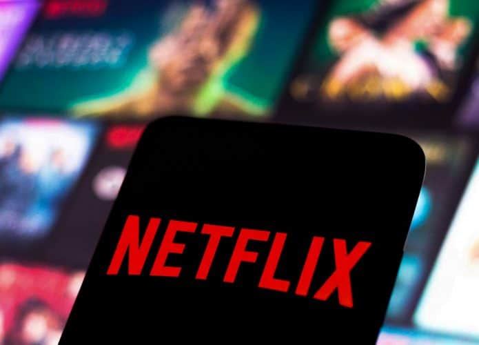 Celular com logomarca Netflix e pôsteres de produções do serviço de streaming ao fundo