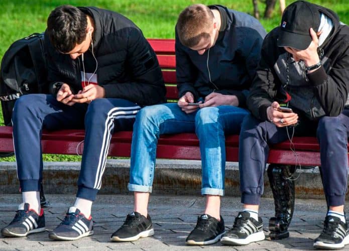 Três rapazes usando smartphone em banco de praça