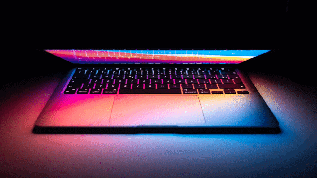 Visão de frente de Macbook parcialmente aberto emitindo luz colorida da tela