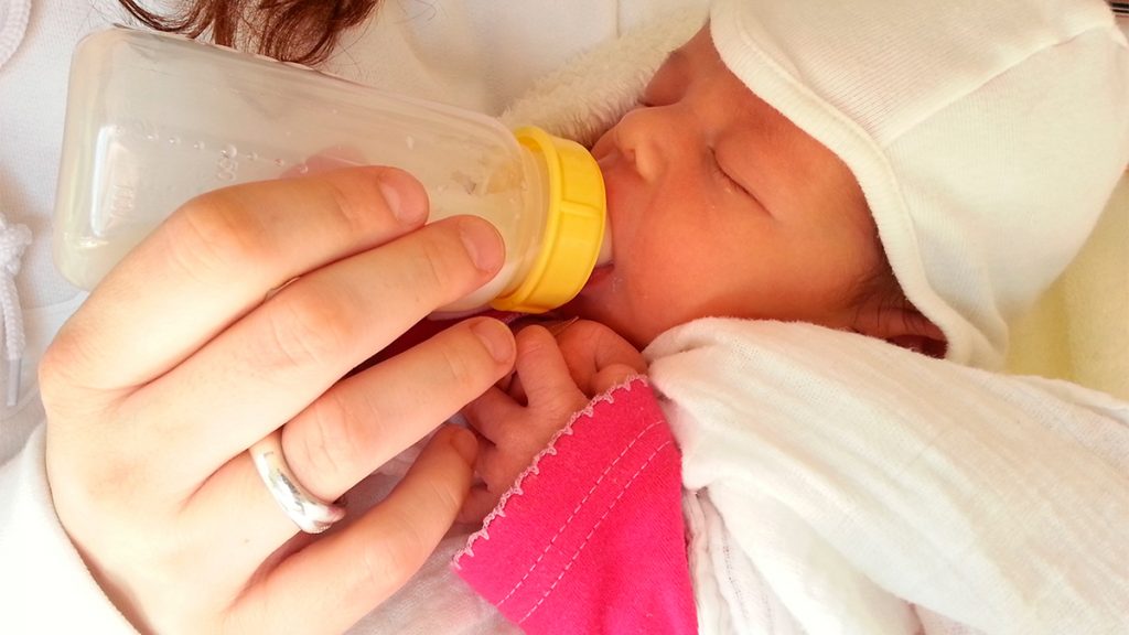 Mãe dando mamadeira para bebê recém-nascido no seu colo