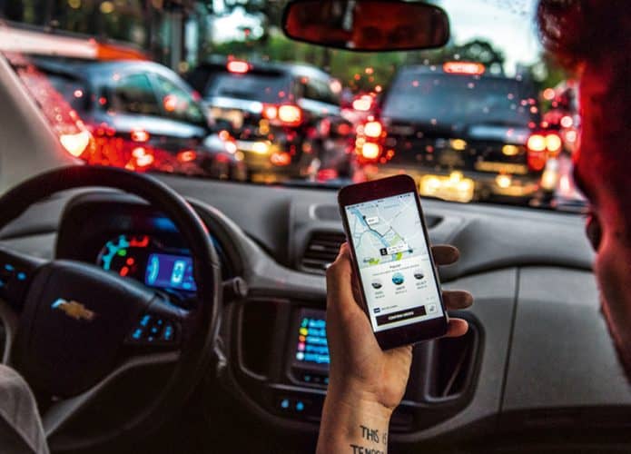 Pessoa com aplicativo do Uber aberto em celular dentro de carro