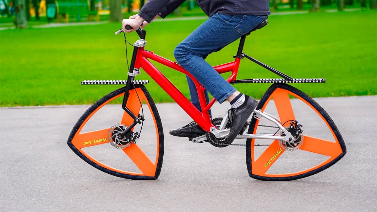 Homem andando em bicicleta com roda triangular num parque