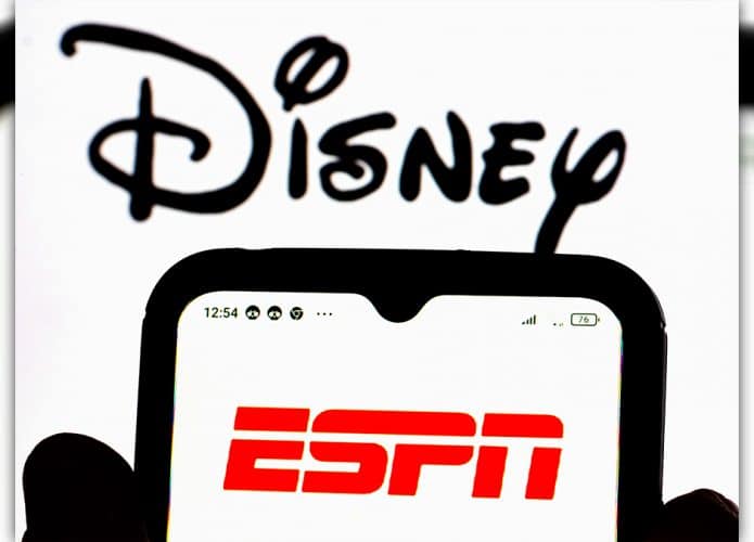 Pessoa segurando celular com logomarca da ESPN e, ao fundo, logomarca da Disney está aberta na tela de um computador