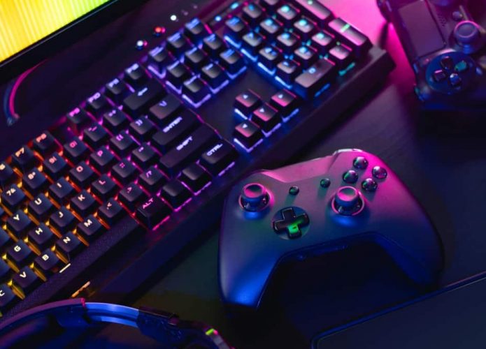 Controle de videogame colocado sobre mesa ao lado de teclado e monitor