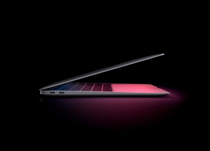 Visão lateral de um MacBook Air parcialmente aberto e com tela acesa emitindo luz rosada