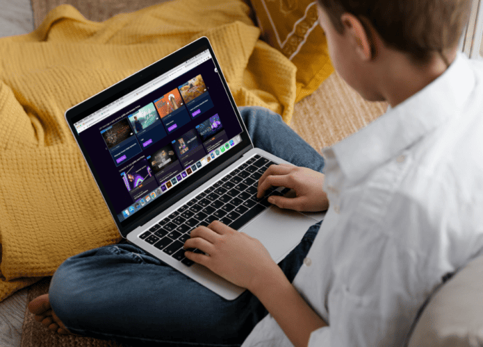 Jovem visto de costas, sentado no sofá, com notebook no colo, selecionando algum jogo dentro da plataforma do Amazon Prime Gaming