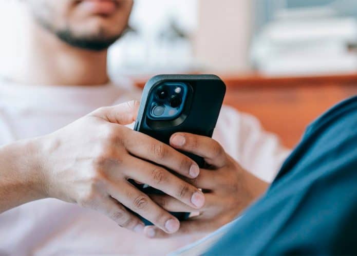 Homem sentado no sofá navegando por redes sociais num iPhone