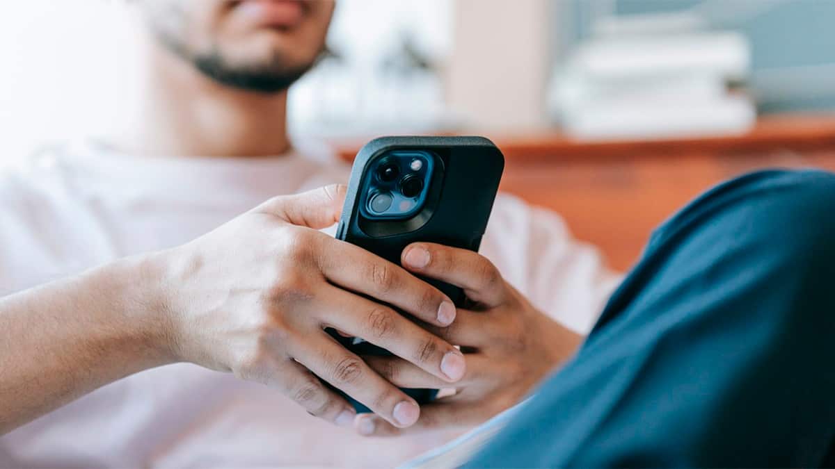 Homem sentado no sofá navegando por redes sociais num iPhone