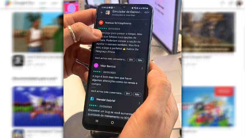 Pessoa segurando celular com página de comentários sobre jogo "Simulador de Escravidão" aberta
