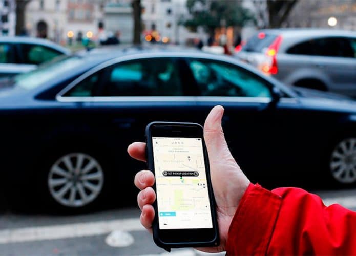 Pessoa com celular na mão esperando, na beira de uma calçada, Uber chegar