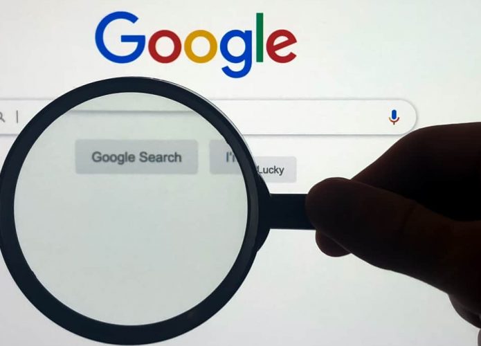Pessoa segurando lupa sobre caixa de pesquisa do Google