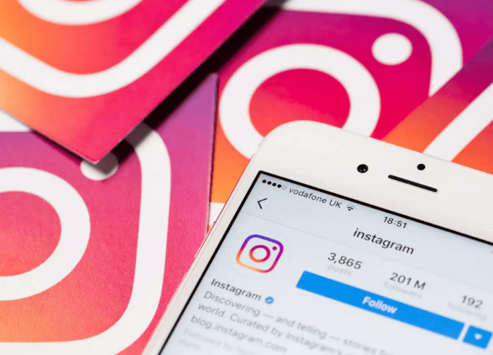 iPhone com página do Instagram no Instagram aberta no aplicativo e, ao fundo, logos do Instagram