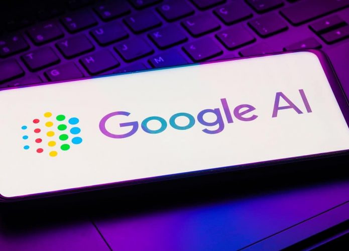 Smartphone com logomarca do Google AI aberta sobre teclado e trackpad de notebook iluminados por luzes coloridas