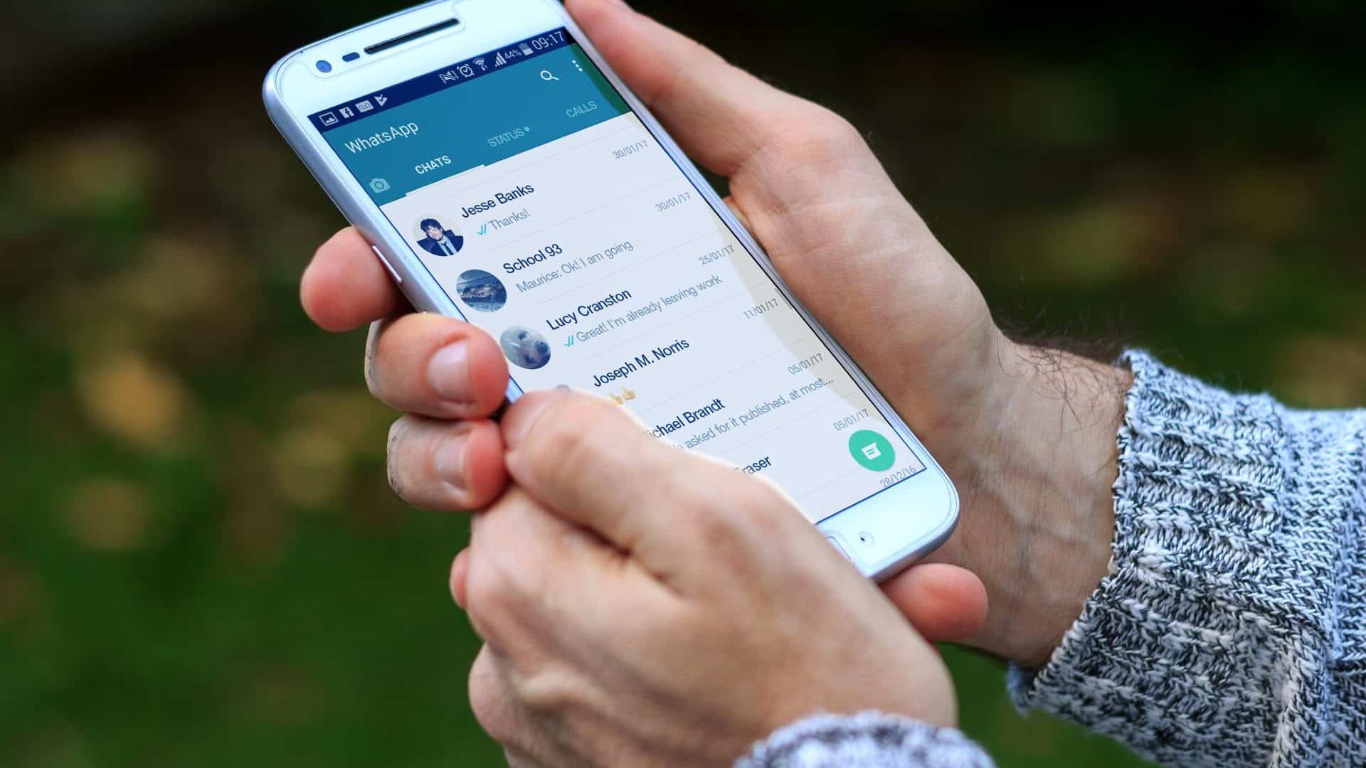 Pessoa segurando celular com lista de conversas do WhatsApp aberta