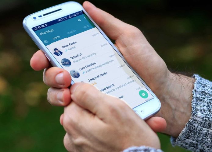 Pessoa segurando celular com lista de conversas do WhatsApp aberta