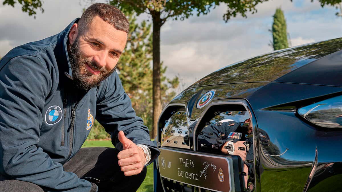 Jogador Karim Benzema agachado em frente BMW i4 M50