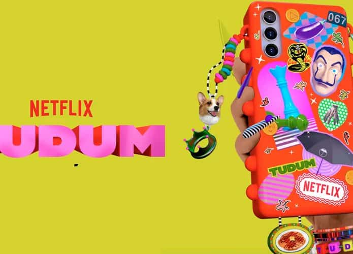 Ilustração de mão segurando celular cheio de adesivos e pingentes de produções da Netflix com logomarca do evento Tudum ao lado