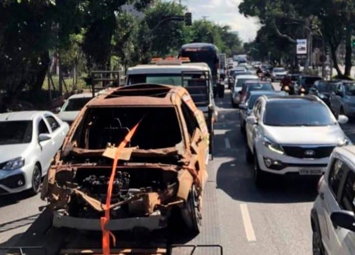 Carcaça de Volvo carbonizado sendo guinchada no meio do trânsito de uma cidade