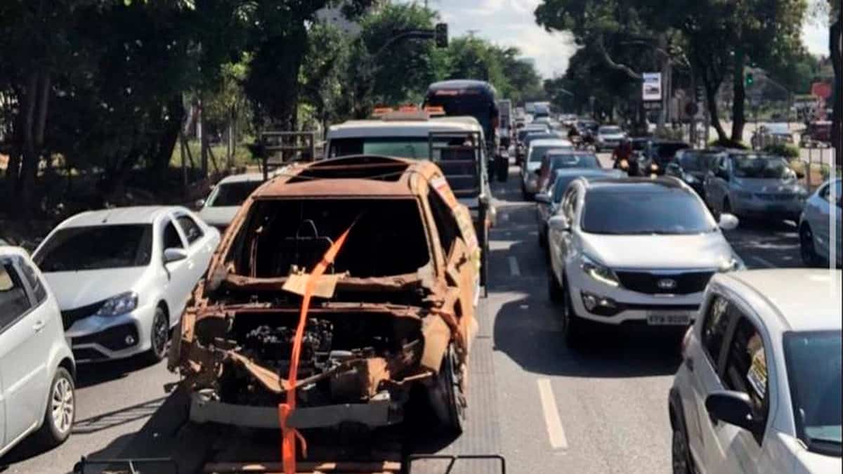 Carcaça de Volvo carbonizado sendo guinchada no meio do trânsito de uma cidade