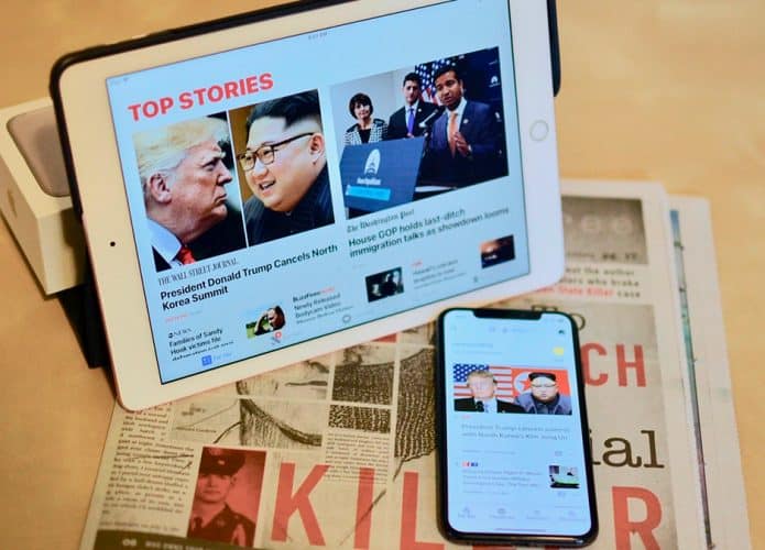 Plataformas de notícias abertas em iPad e iPhone, colocados sobre um jornal