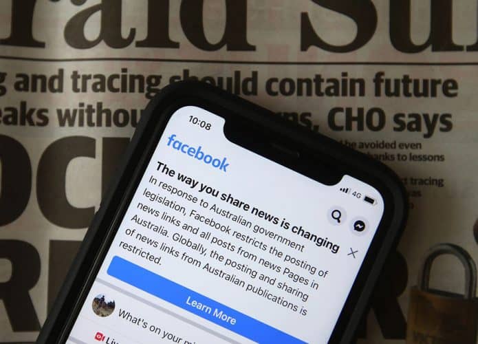 Aviso do Facebook sobre mudança no compartilhamento de notícias aberto num iPhone, colocado sobre um jornal