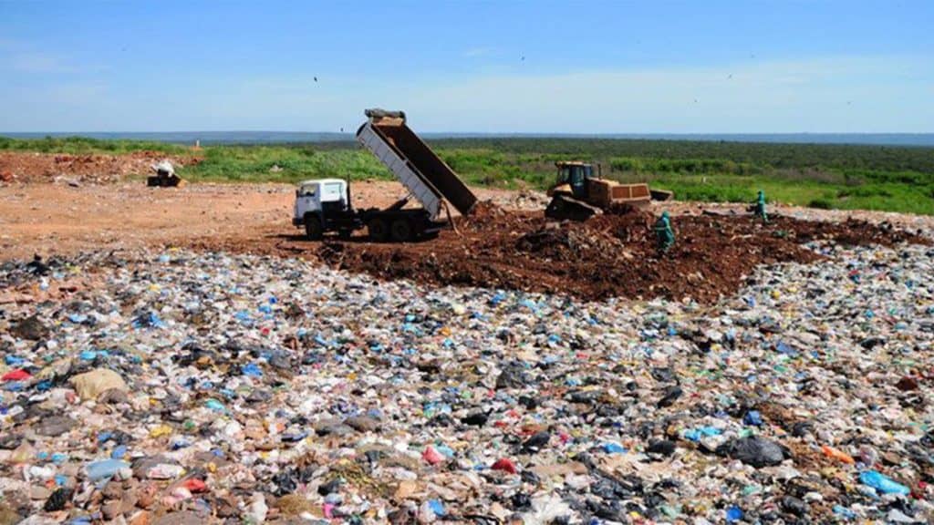 Caminhão despejando lixo em lixão com pessoas e abutre em volta