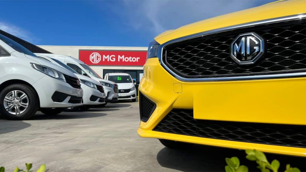 Close em símbolo da marca MG na grade de um carro amarelo estacionado numa concessionária da marca