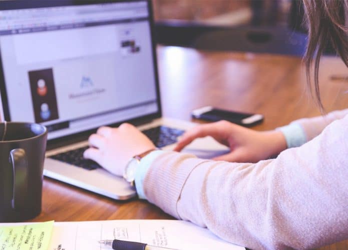 Pessoa usando notebook em cima de mesa com papeis e celular em volta