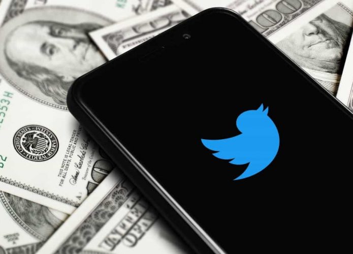 Celular com logomarca do Twitter na tela colocado sobre notas de dólares para ilustrar cobrança de API do Twitter