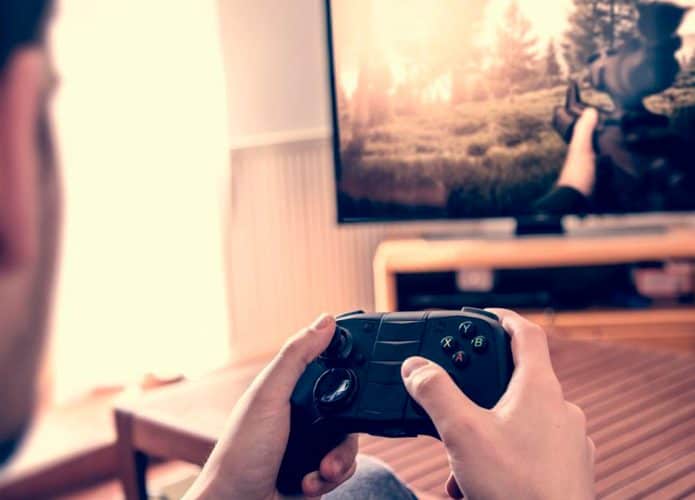 Homem sentado no sofá segurando controle de videogame enquanto joga na sala olhando para a TV