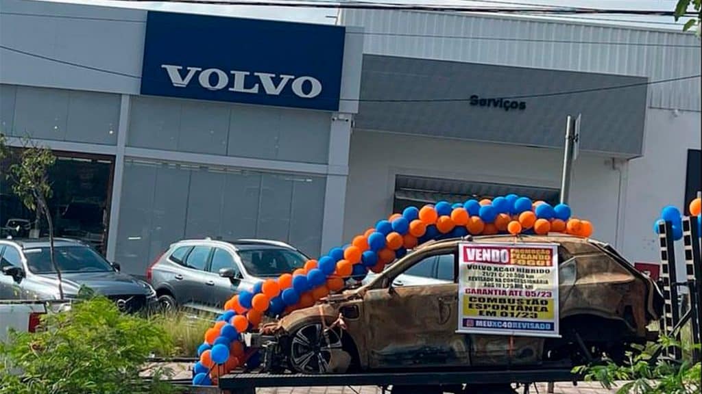 Carcaça de Volvo queimado com bexigas e banner, estacionada em frente uma concessionária da marca