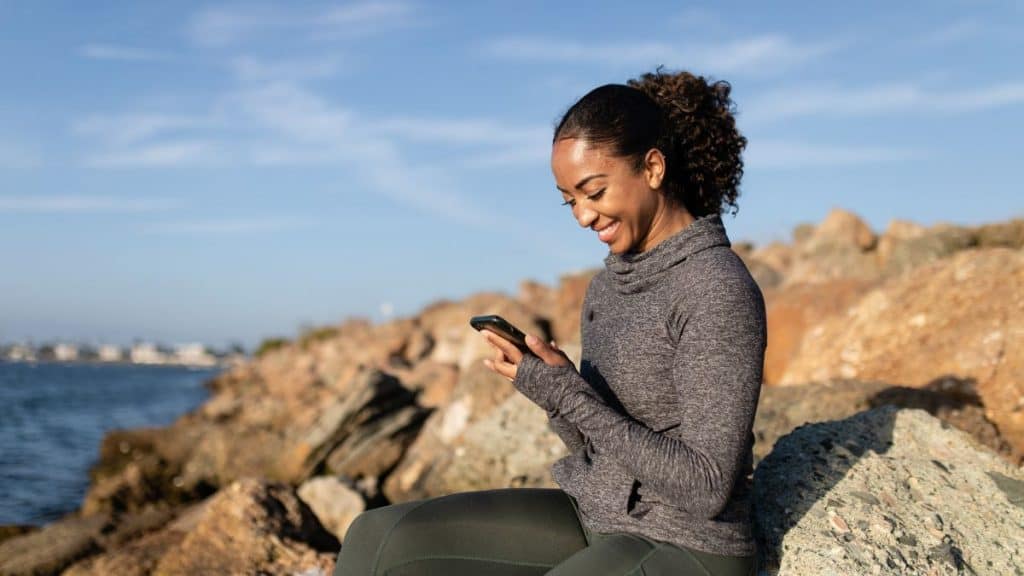 mulher com celular em uma pedra com mar de fundo