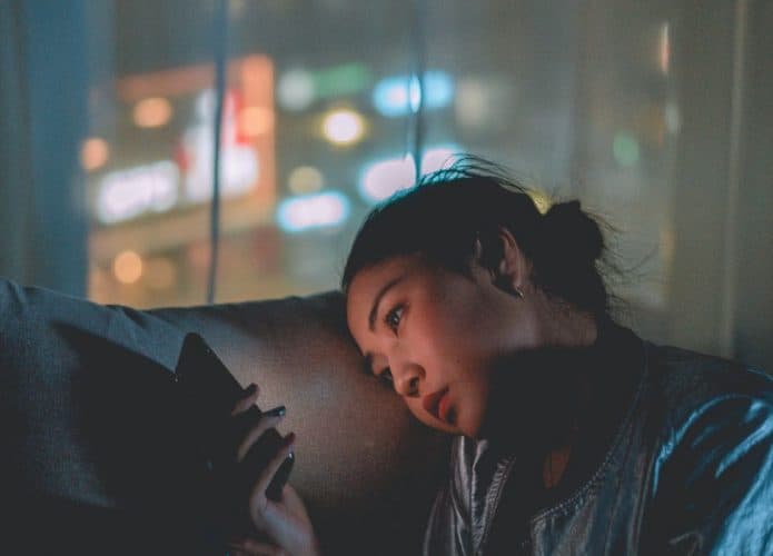 Mulher com celular no sofá e semblante triste