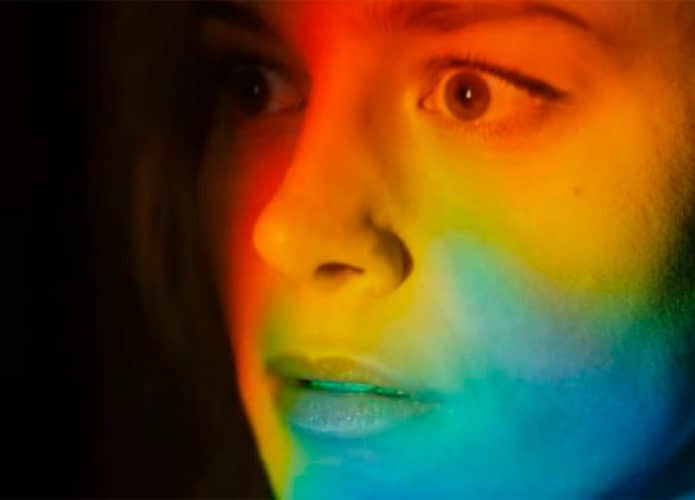Rosto de Brie Larson com expressão surpresa iluminado por luz colorida