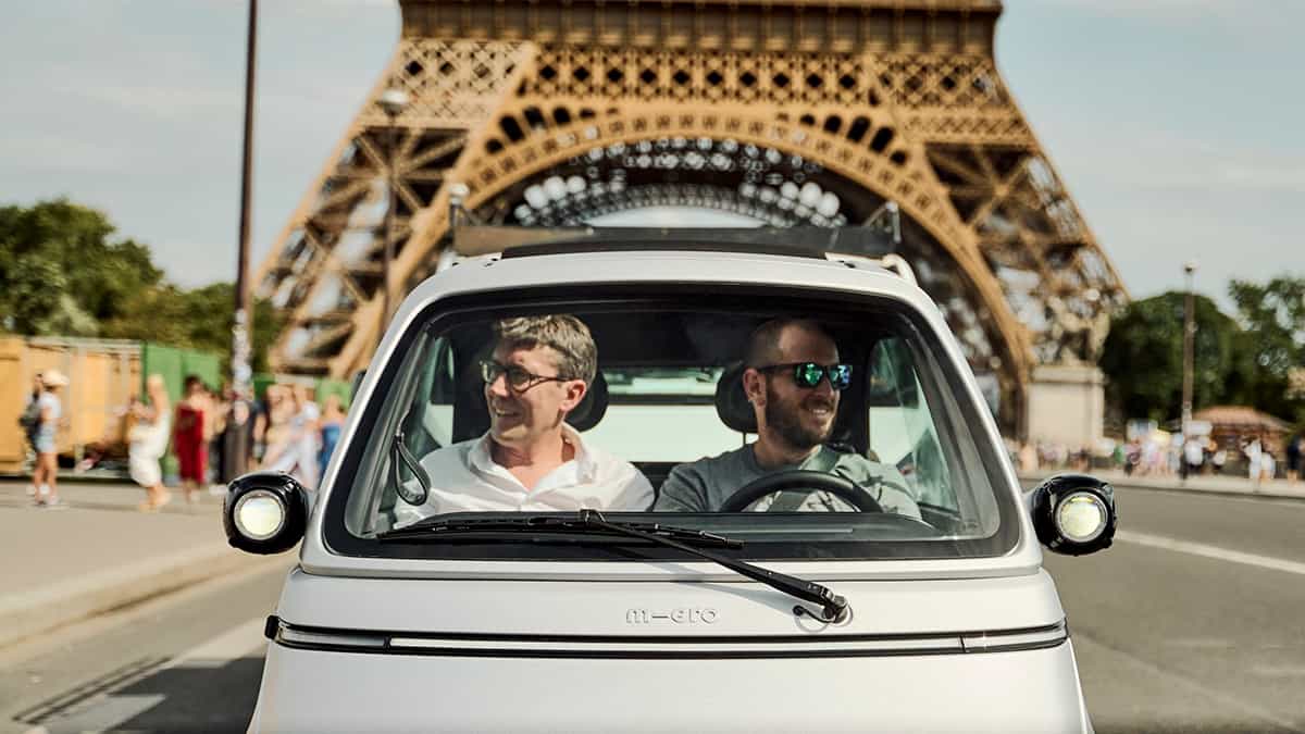 Homens dirigindo Microlino em Paris, perto da Torre Eiffel