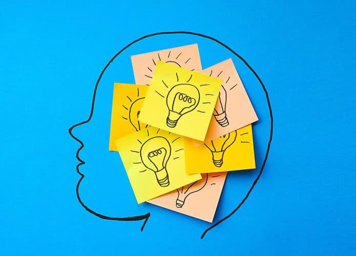 Ilustração de post-its com desenho de lâmpada colados uns sobre os outros na mente de uma pessoa