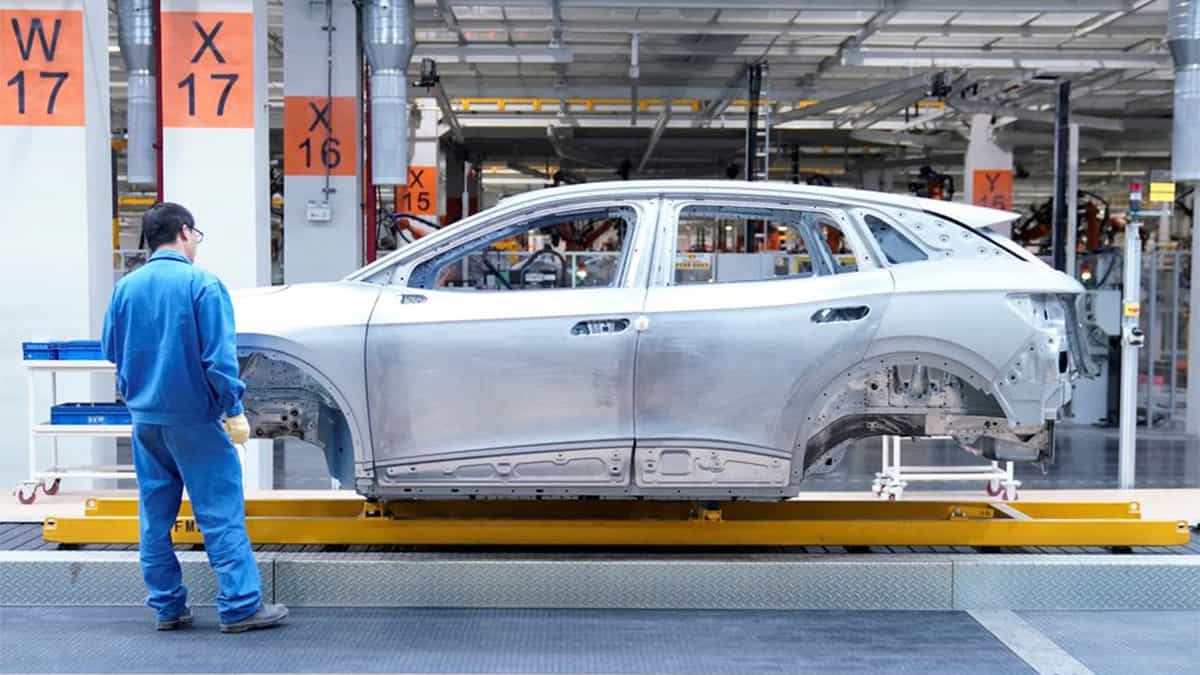 Homem em pé ao lado de carcaça de carro numa das montadoras chinesas