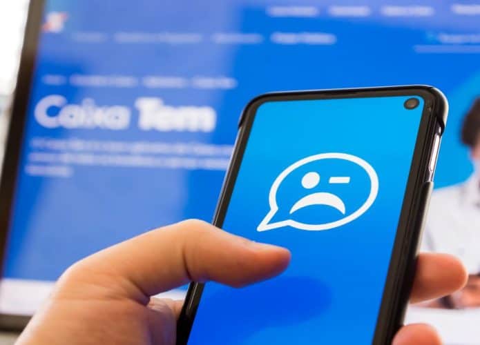 Imagem de alguém segurando celular com app do Caixa tem com ícone com um careta