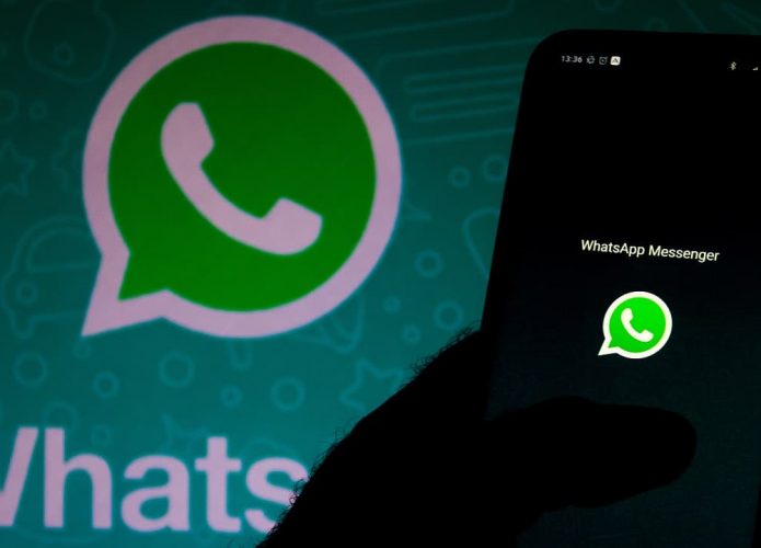 Pessoa segurando celular com logomarca do WhatsApp e, ao fundo, logomarca do WhatsApp