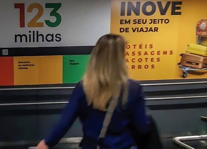 Mulher de costas passando por anúncio da 123 Milhas