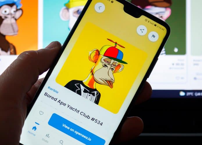 Pessoa segurando celular com um dos NFTs da Bored Ape aberto e, ao fundo, está o catálogo de NFTs da Bored Ape