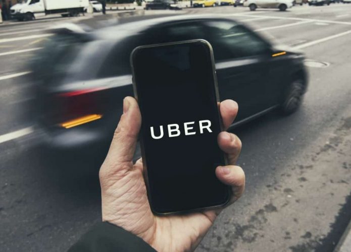 Pessoa segurando celular com logomarca da Uber enquanto carro passa atrás